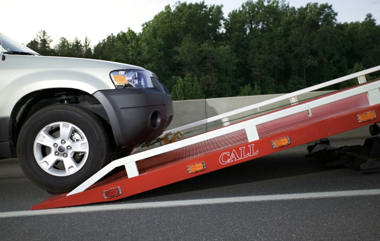 Silver SUV driving up a red flatbed tow truck ramp for heavy duty towing in Bay Shore, NY