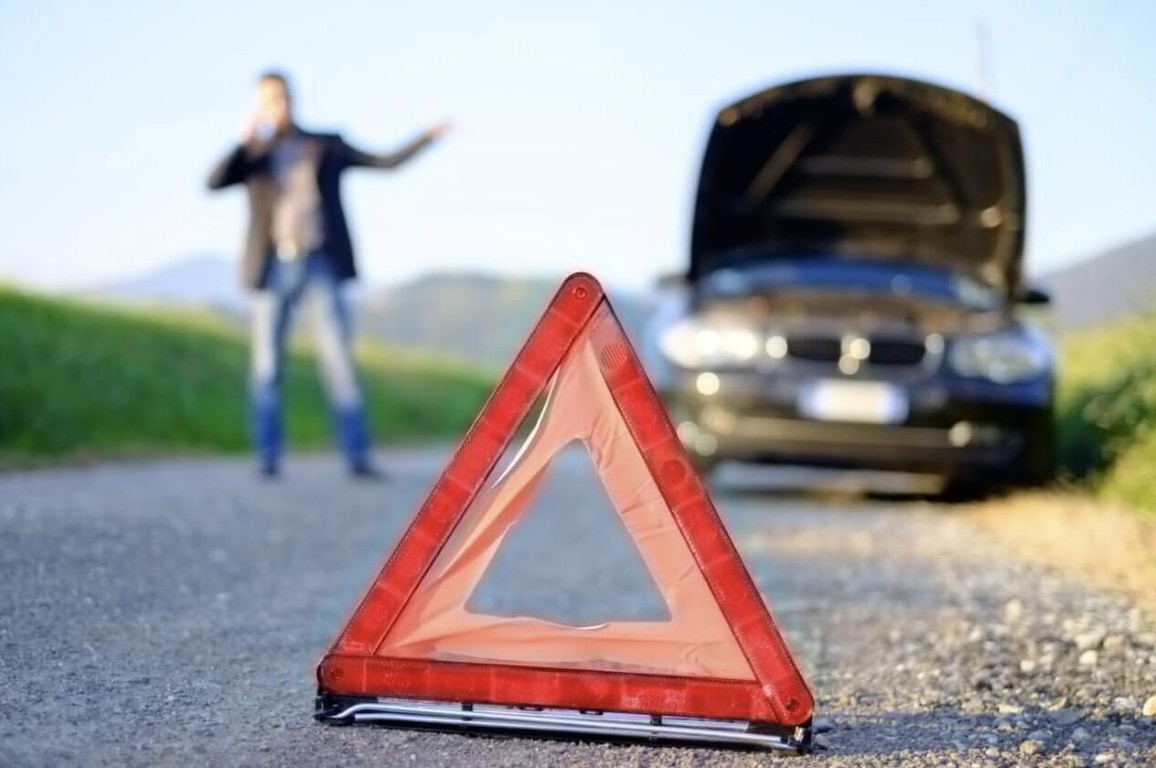 Red warning triangle on roadside with broken down car and driver calling for winch out service in Bay Shore, NY